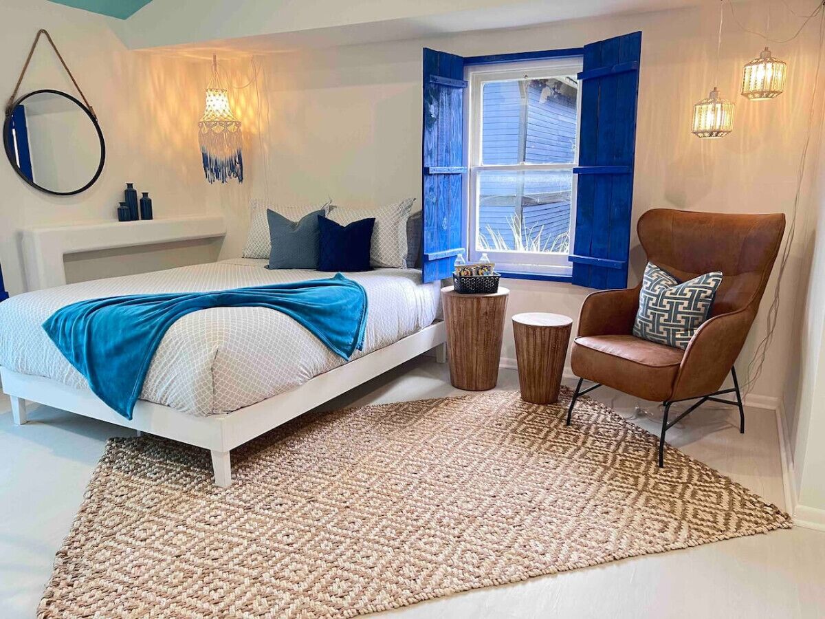 Een slaapkamer met een bed, een stoel, een raam met blauwe luiken en een wandlamp.