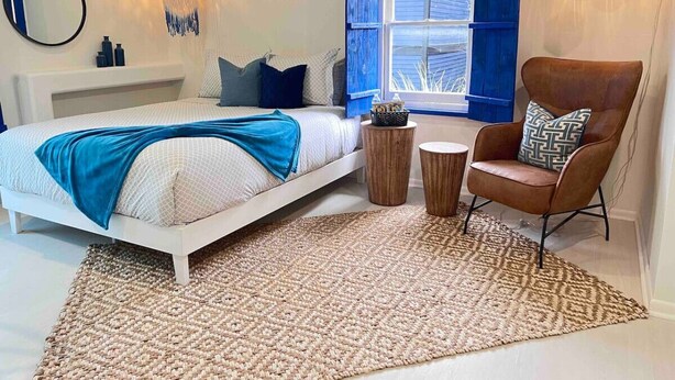 A bedroom with a bed, a chair, a window with blue shutters, and a wall-mounted light fixture.