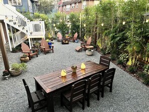 Een houten terras met een tafel en stoelen, omgeven door potplanten en een bamboomschutting.
