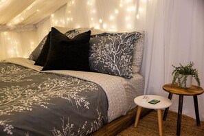 Ein Schlafzimmer mit einem Bett, Kissen, einem Nachttisch mit einem Buch und einer Topfpflanze.