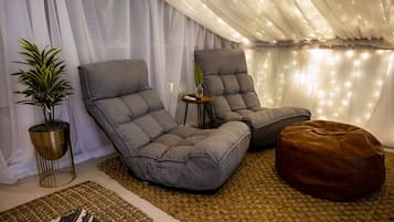 Un rincón acogedor con dos sillones grises, una mesita auxiliar, una planta en maceta y un reposapiés marrón.