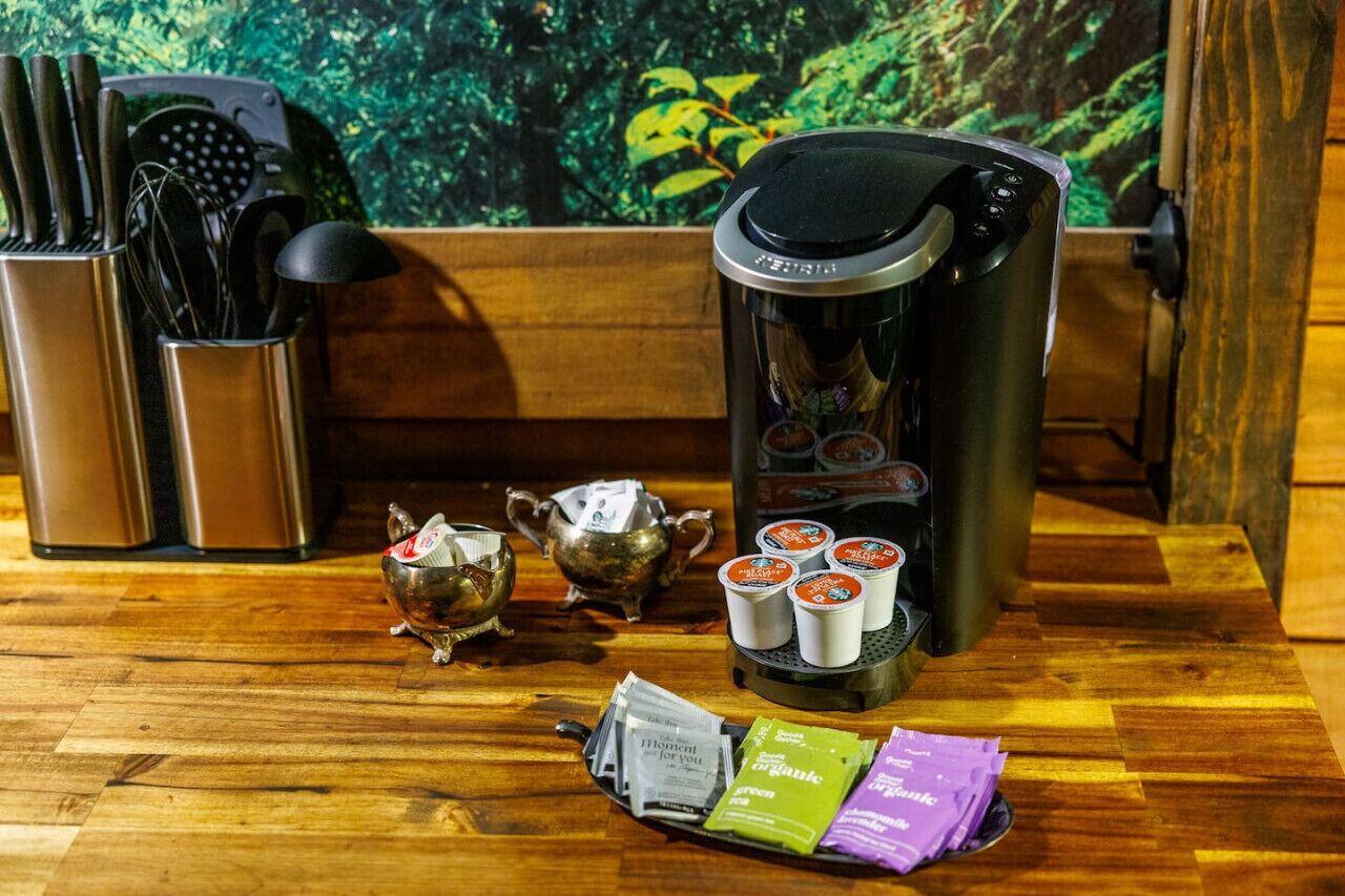 En kaffestation med kaffemaskine, tepotter, kopper og kaffekapsler på et træbord.
