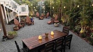 Eine Terrasse im Freien mit einem Holztisch und Stühlen, umgeben von Kübelpflanzen und einer Feuerstelle.