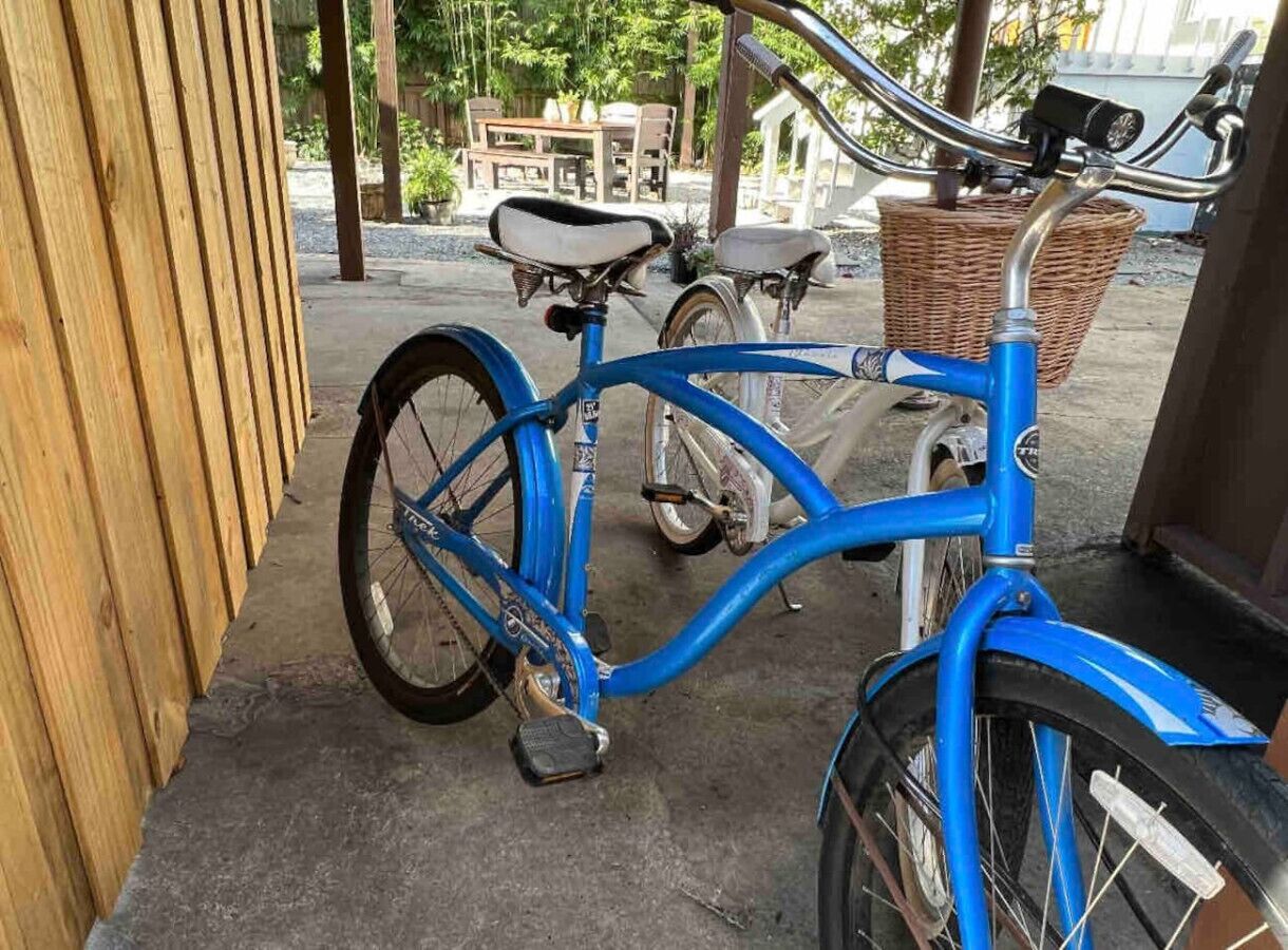 A blue bicycle parked outside a building with a wooden fence and a wicker basket attached to the handlebars.