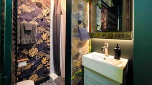 Ein Badezimmer mit Steinwand, Waschbecken, Spiegel und einer Duschvorhang mit Blumenmuster.