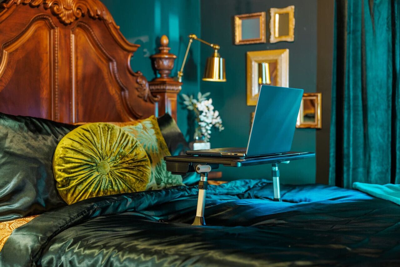 Een bed met een laptop op een standaard, een houten hoofdbord en een decoratieve lamp.