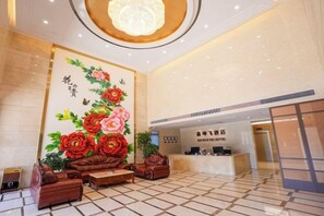 Um saguão de hotel com balcão de recepção, um grande mural floral e um lustre.