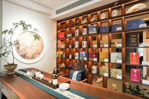 Uma área de recepção com uma estante de madeira repleta de livros e objetos decorativos, um espelho redondo e um conjunto de chá tradicional sobre uma mesa de madeira.