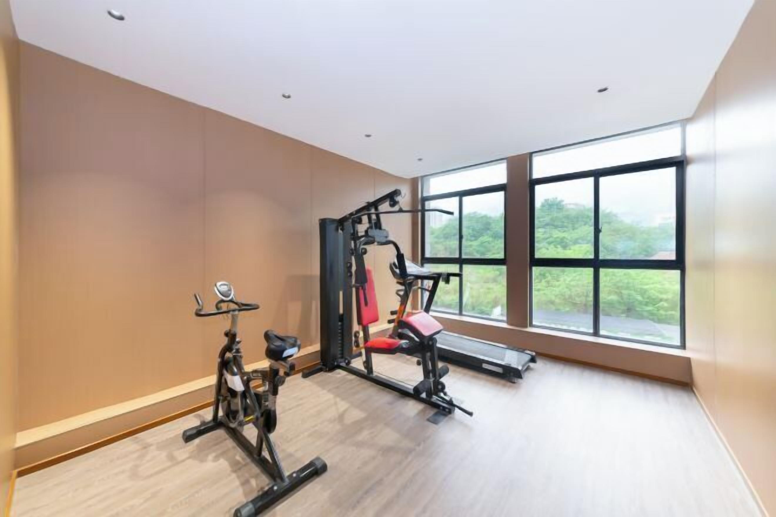 Un gimnasio con equipo de ejercicio, ventanas amplias y vistas a zonas verdes.