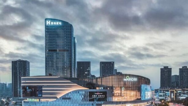 Un hotel moderno con fachada curva, un llamativo letrero del hotel H y una gran pantalla digital que muestra el nombre del hotel.