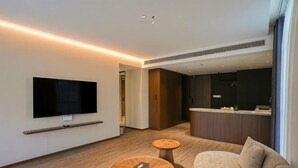Habitación de hotel moderna con televisor de pantalla plana, un sofá, dos mesitas de madera y un mostrador de recepción.