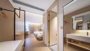Una habitación de hotel moderna con una cama grande, un baño con espejo y lavamanos, y un pasillo que conduce a otra habitación.