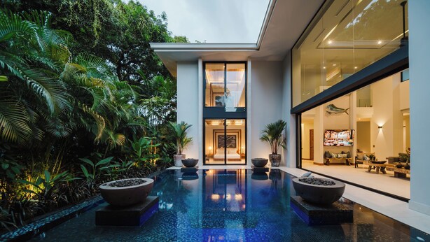 Ein modernes Haus mit Glasfassade, einem Swimmingpool und üppiger Bepflanzung.