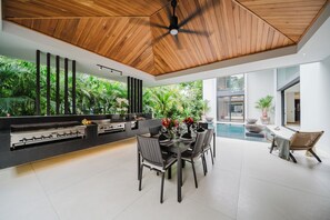 A modern kitchen with a built-in grill, dining area with chairs, and a view of lush greenery.