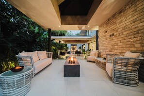 A modern outdoor living area with a fire pit, sofas, and wicker chairs.