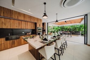 A modern kitchen with wooden cabinets, a marble island, and a dining area with bar stools.