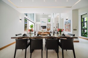A spacious dining area with a long table, black upholstered chairs, and a view of a living room in the background.