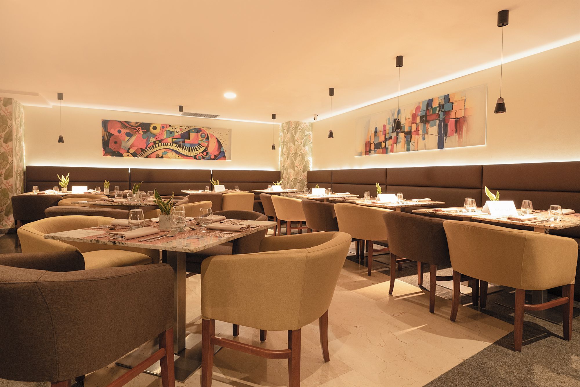 Ein Restaurant mit Sitzgelegenheiten in Form von Boxen und Tischen, jeweils mit Besteck und Gläsern gedeckt, und einem großen, abstrakten Gemälde an der Wand.