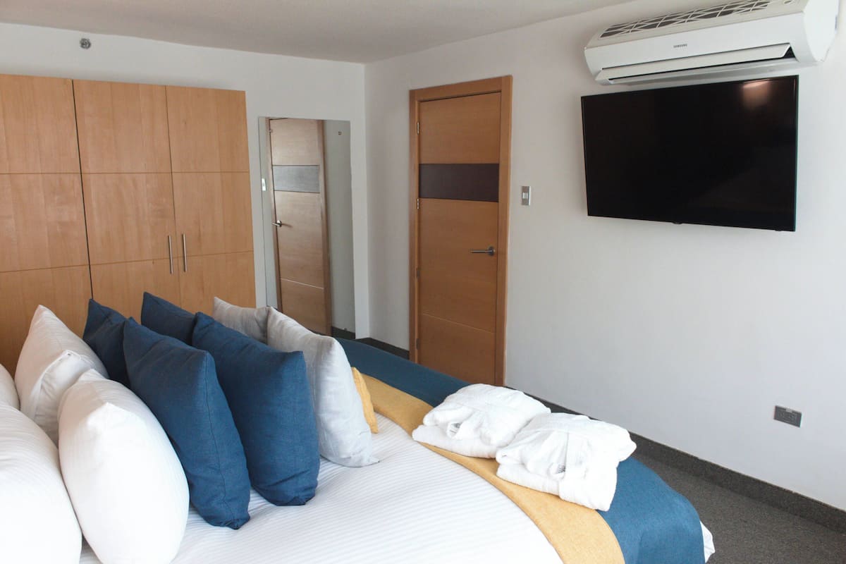 A hotel room with a bed, pillows, a wardrobe, a door, and a wall-mounted TV.