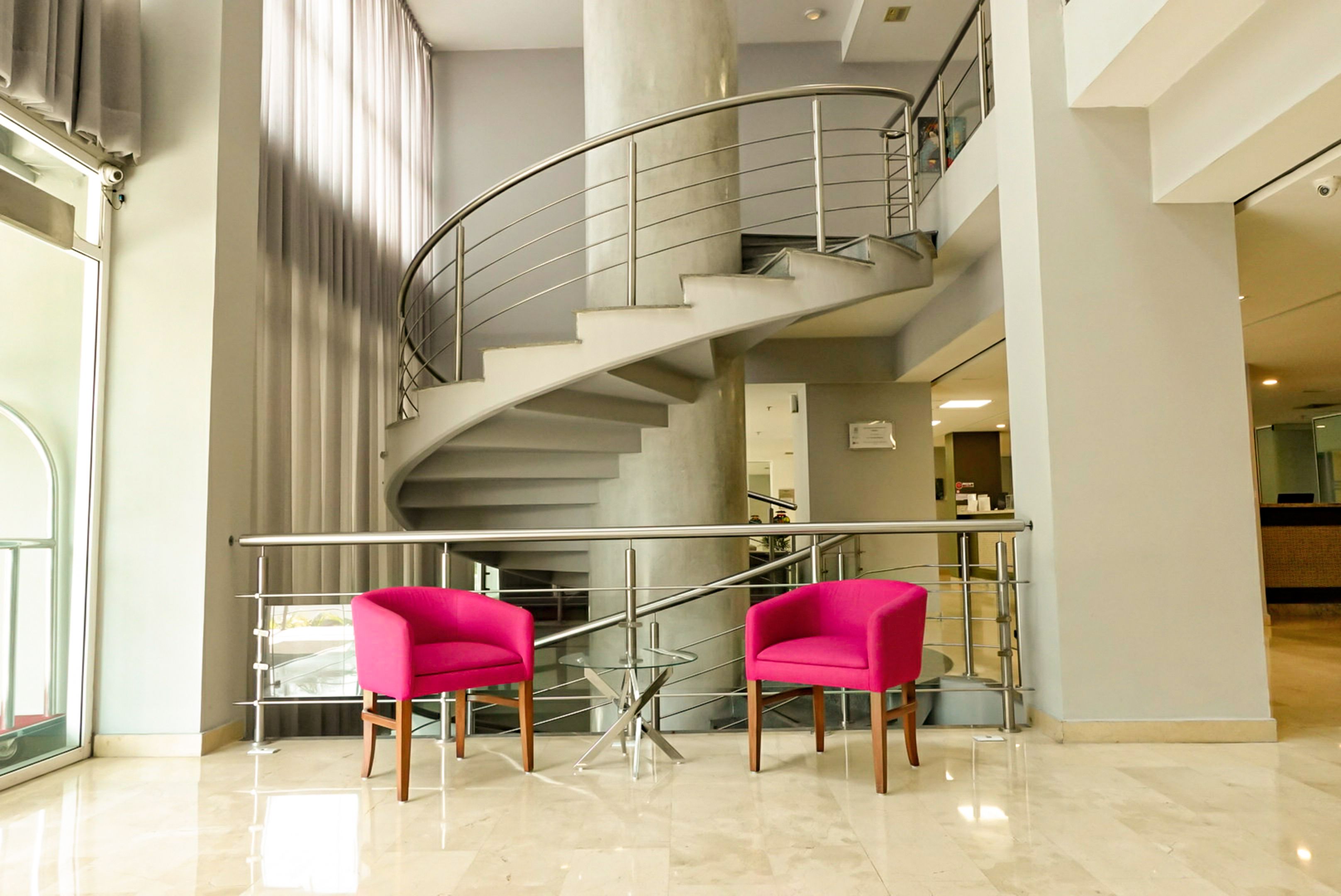 A modern interior with a spiral staircase, two pink chairs, and a glass railing.