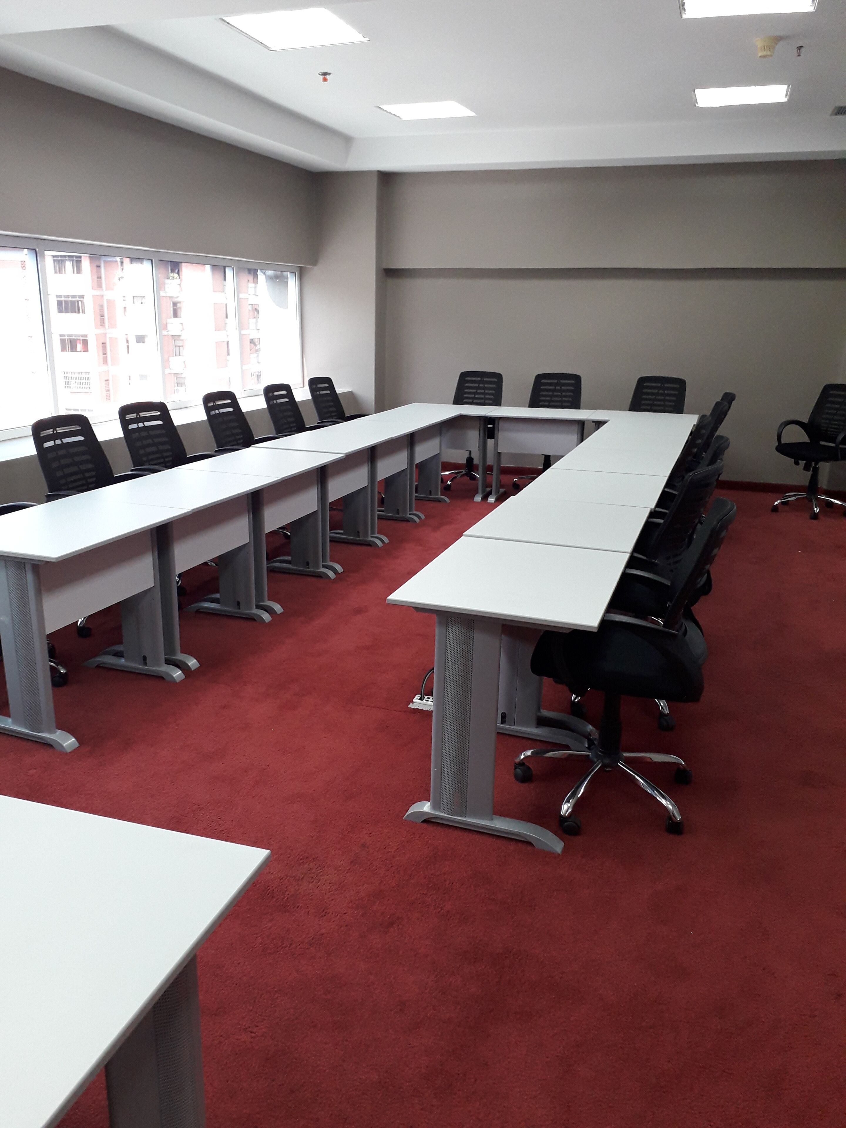 A conference room with a long table, multiple chairs, and a red carpeted floor.