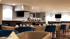 A hotel dining area with tables and chairs, a buffet setup, and a television screen. - Hesperia Maracay (Maracay)