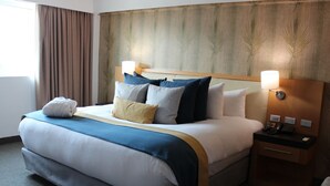 A hotel room with a large bed, a wooden headboard, two bedside tables with lamps, and a window with curtains. - Hesperia Maracay (Maracay)