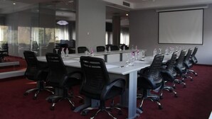 A conference room with a long table, black chairs, and a projector screen. - Hesperia Maracay (Maracay)