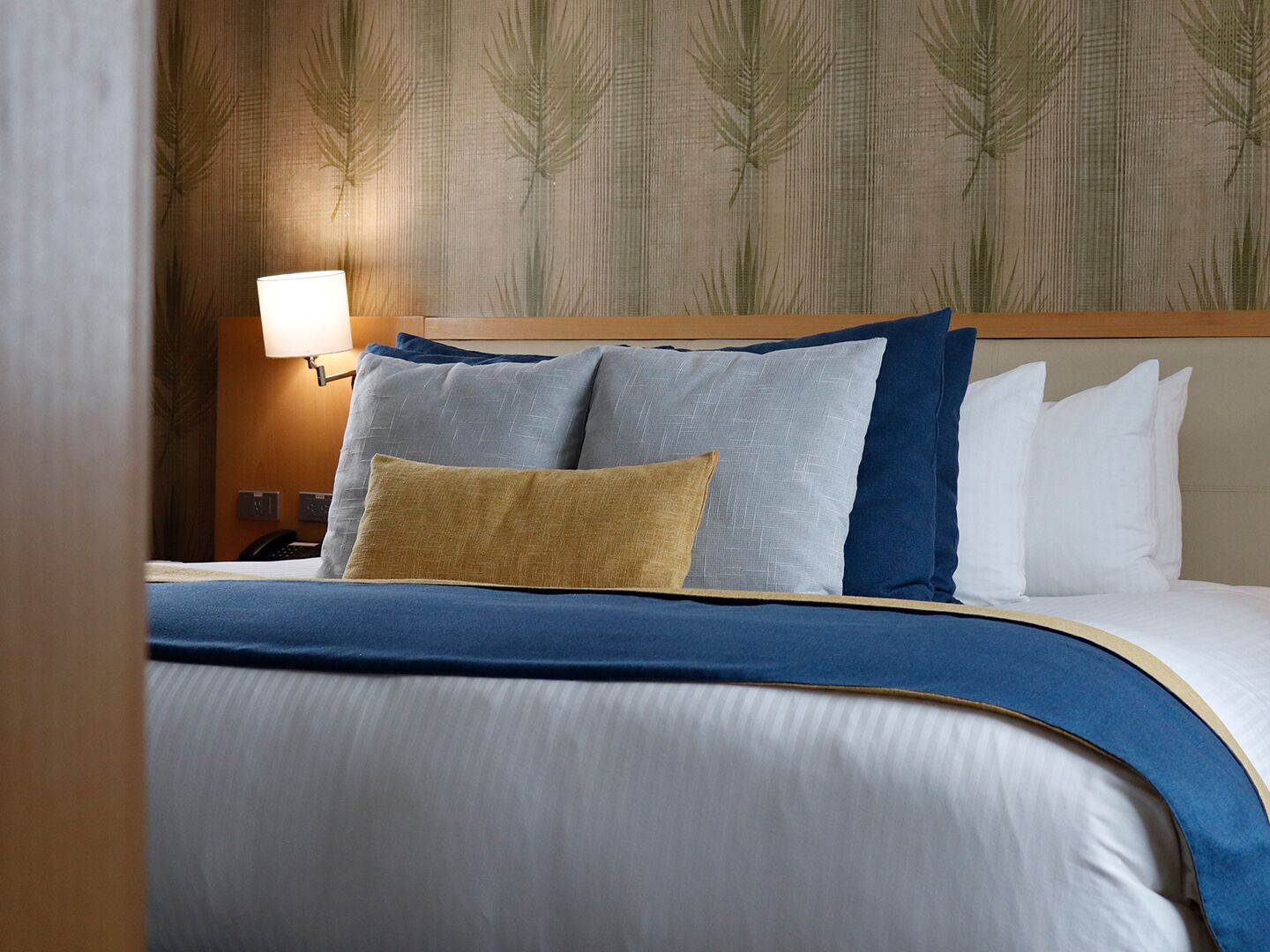 A neatly made bed with a blue and white duvet, two pillows, and a bedside lamp.