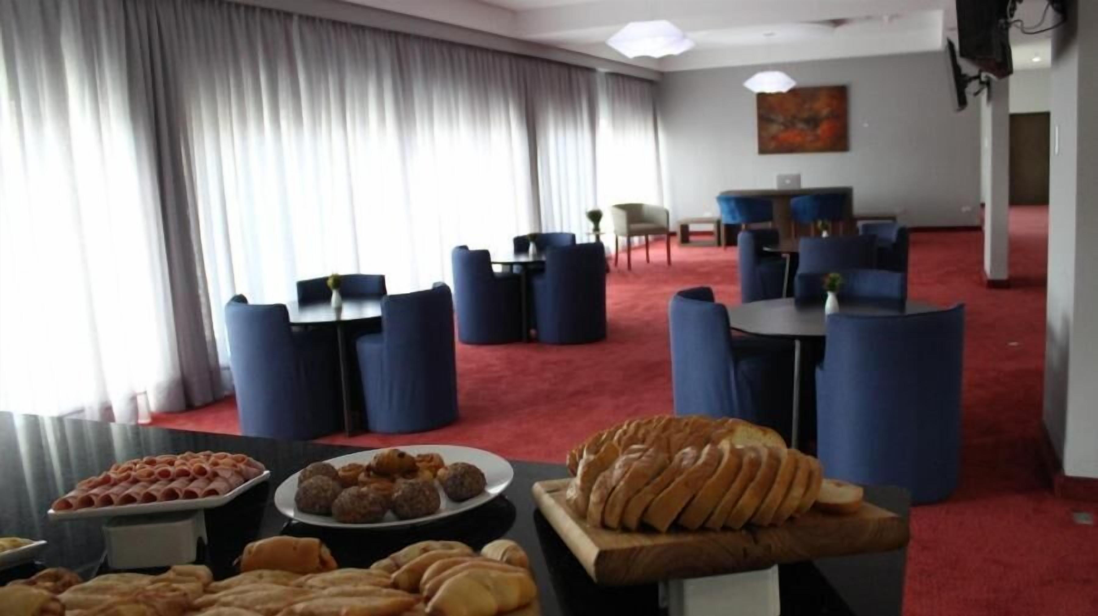 A hotel room with a red carpet, a dining area with blue chairs and tables, and a buffet with various food items.