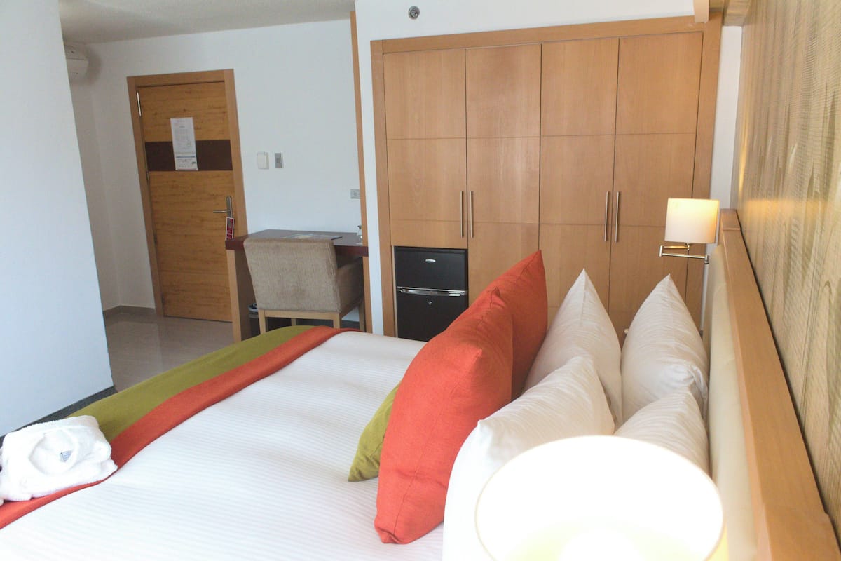 A hotel room with a bed, a desk, a wardrobe, and a lamp.