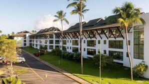 A modern hotel with a white facade, large windows, and a covered outdoor area with palm trees. - Apartamento Luxo no Beach Class Resort Muro Alto 3204 (Ipojuca)
