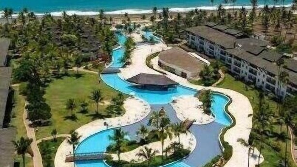 A resort with a central swimming pool, palm trees, and a beach view. - Apartamento Luxo no Beach Class Resort Muro Alto 3204 (Ipojuca)