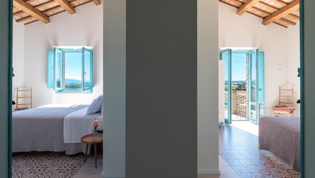 A bedroom with a bed, a small table, and a window with a view.