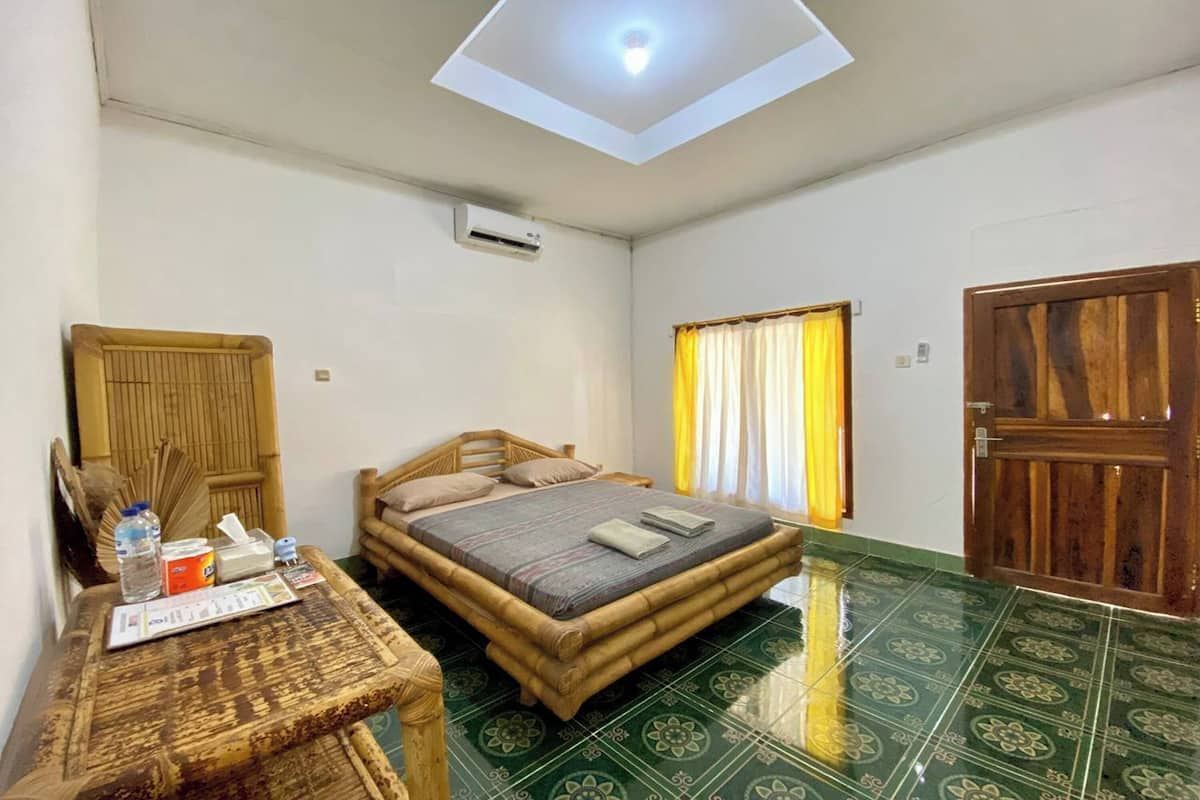 Una stanza con un letto, un tavolo con una bottiglia e fazzoletti, una finestra con tende e una porta.