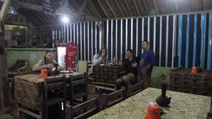 A rustic interior with wooden furniture, a patterned tablecloth, and a sign on the wall. - Duyung Rooms and Resto by Zuzu (Kuta)