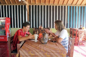A dining area with a table, chairs, a patterned tablecloth, a vase, and a Coca-Cola refrigerator. - Duyung Rooms and Resto by Zuzu (Kuta)