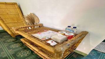 A room with a woven bench, a wall-mounted fan, a menu, a tissue box, and bottled water.