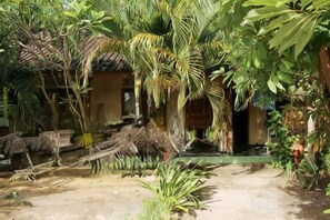 A tropical garden with a thatched-roof structure, surrounded by various plants and a dirt path. - Duyung Rooms & Resto Gerupuk (Kuta)