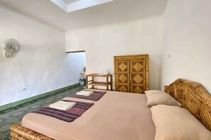 A bedroom with a bed, a wooden wardrobe, a small table, and a wall-mounted light fixture. - Duyung Rooms & Resto Gerupuk (Kuta)