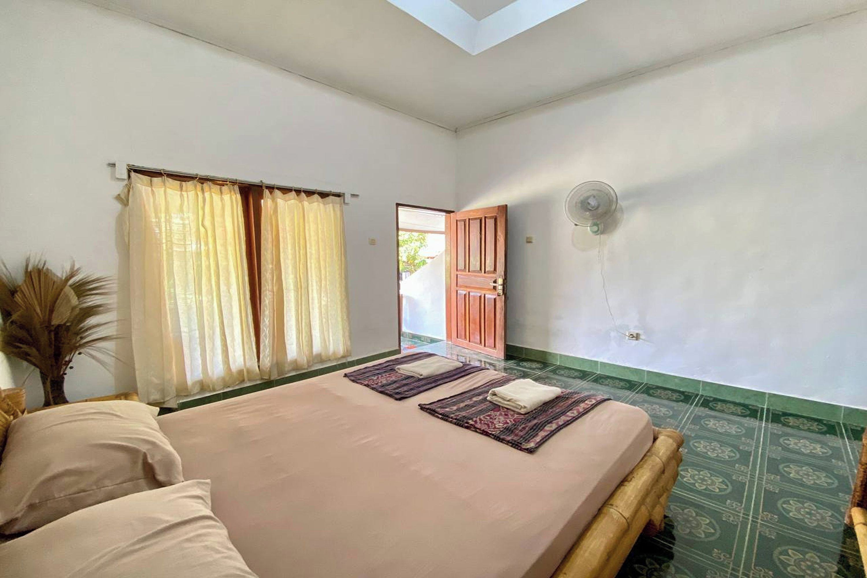 Un dormitorio con cama, ventana con cortinas, puerta y un ventilador fijado a la pared.