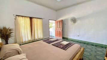 Un dormitorio con cama, ventana con cortinas, puerta y un ventilador fijado a la pared.