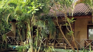 A building surrounded by lush tropical vegetation, with a tiled roof and a wooden fence. - Duyung Rooms and Resto by Zuzu (Kuta)