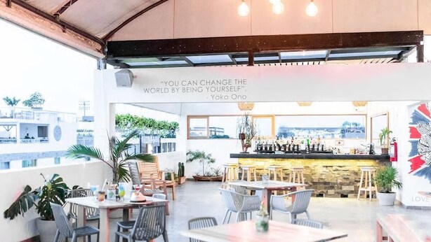An outdoor café with tables and chairs, a bar area, and a quote on the wall. - Soho Playa (Playa del Carmen)