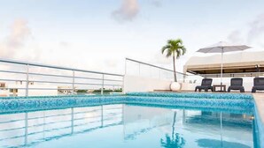 A rooftop pool with clear blue water, a palm tree, and lounge chairs under a large umbrella. - Soho Playa (Playa del Carmen)