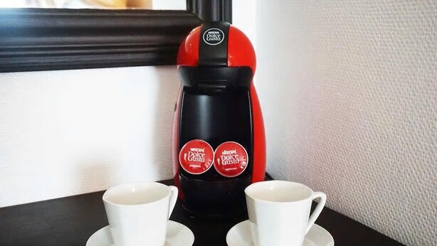 Punainen ja musta Dolce Gusto -kahvinkeitin, jonka päällä pöydällä on kaksi valkoista kuppia.