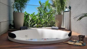 Un bain à remous installé dans un petit espace extérieur doté d’un plancher en bois, entouré de plantes en pot et agrémenté d’une lampe.