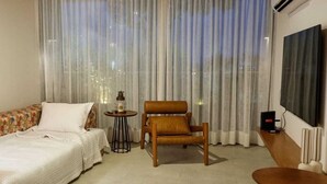Une chambre à coucher avec un lit, une chaise, une petite table et une grande fenêtre avec des rideaux.