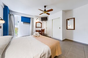 Habitación de hotel con cama, ventilador de techo, televisor, escritorio con silla y ventana con cortinas.