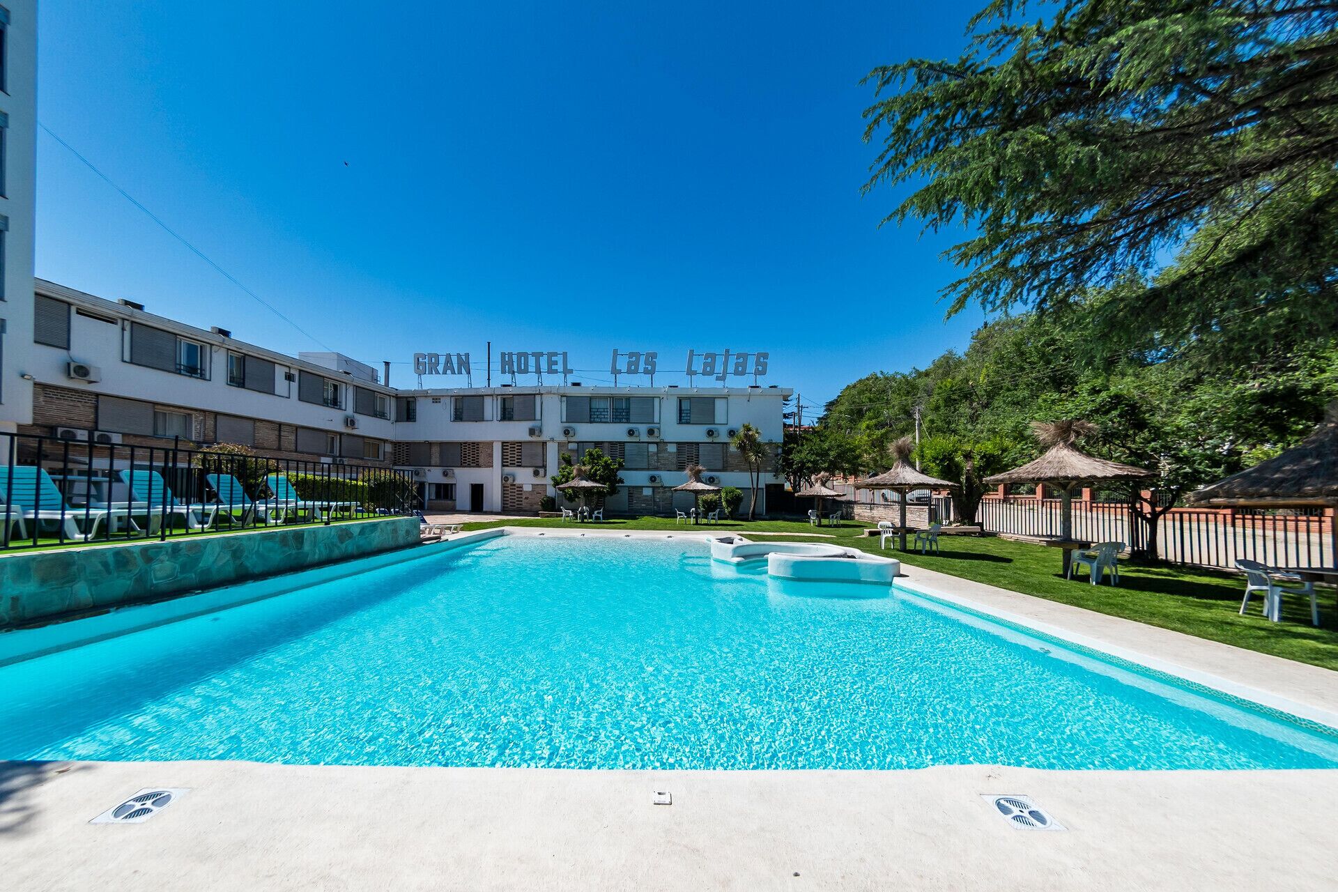Un hotel con piscina, mobiliario exterior y un cielo azul despejado.